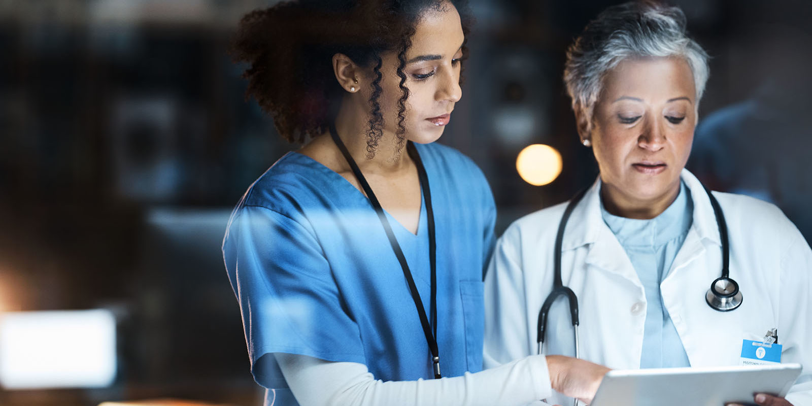 Enfermera y doctora revisando datos de paciente con MedWorks en tablet para turno de noche.
